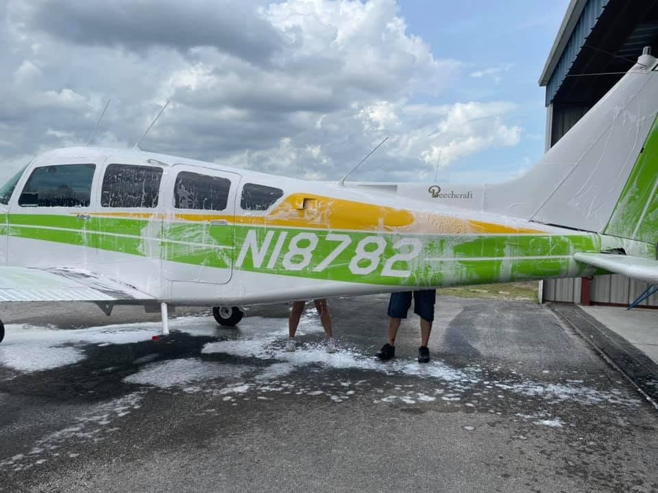 Beechcraft single-engine aircraft covered in soap suds during a hand wash at an airport hangar